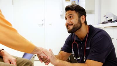 En läkare som ler och håller en man i handen.