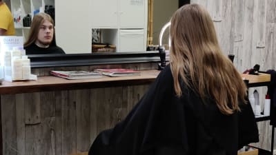 En ung man med långt hår sitter i en frisörstol.