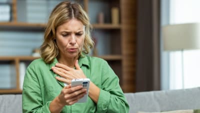 Kvinna sitter i en soffa och ser chockerat på sin mobil