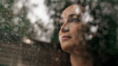 Katja Lahti seisoo sisällä kotonaan ja katsoo ulos ikkunasta, jossa on sateen jäljiltä vesipisaroita.