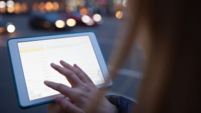 En kvinna håller i en datortablett med touchscreen på en mörk stadsgata.