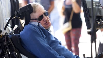 Närbild på Stephen Hawking ute i solskenet med solglasögon. 