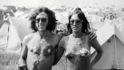 Ett hippiepar med bar överkropp poserar framför tält år 1967.