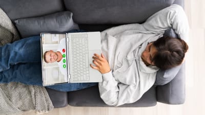en kvinna ligger i en soffa och har en dator i famnen som hon videochattar med 
