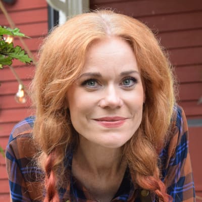 Ella ler mot kameran ute på verandan. Hon har flätat sitt röda hår.