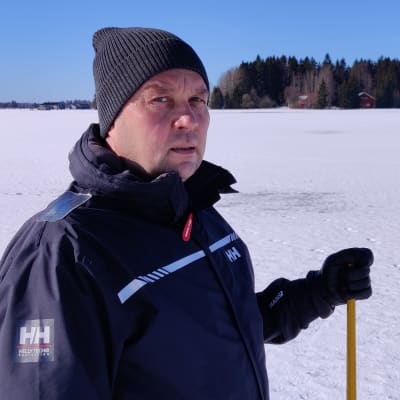 Mies seisoo lumisella pellolla ja katsoo vakavan näköisenä kohti kameraa.