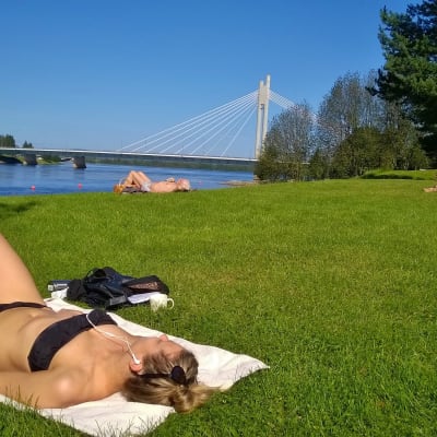 Nainen ottaa aurinkoa Rovaniemen Ounaskosken rannalla.