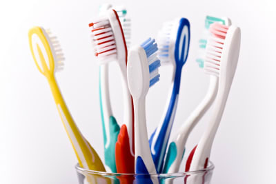 Sju tandborstar i olika färger står i ett tandglas