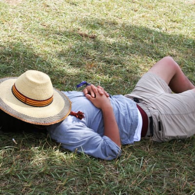 Man som ligger på gräset med en hatt över ansiktet.