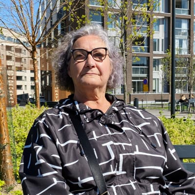 Mirva Alanko sitter i solen på en bänk framför bostadshus.