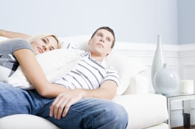 Ung man och kvinna ligger på en soffa, hon kramar honom men han tittar bort