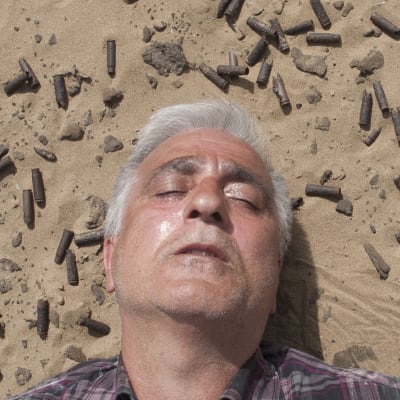 Saeid Sadeghi ligger i sanden omgiven av patronhylsor.