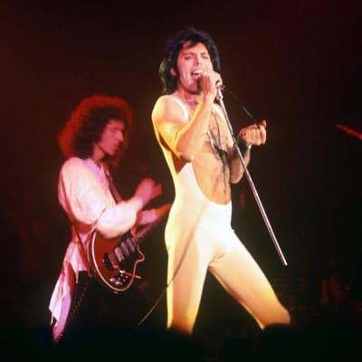Brian May och Freddie Mercury i Queen live 1977. Mercury har vit jumpsuit.