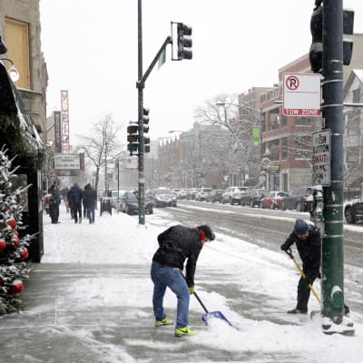 Kaksi miestä lapioi lunta kaupungin kadulla
