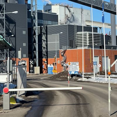 Rök stiger från taket på en del av byggnaden som är en pappersfabrik. I förgrunden syns en bom som hindrar obehöriga att köra in på området.