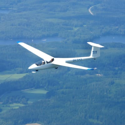 Ett ultrlalätt flygplan flyger över en skog, två sjöar syns i bakgrunden