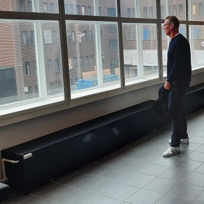Medelålders man står och tittar ut genom ett stort fönster.