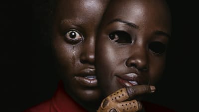 En svart kvinna med skräckslagen blick täcker halva ansiktet med en mask.
