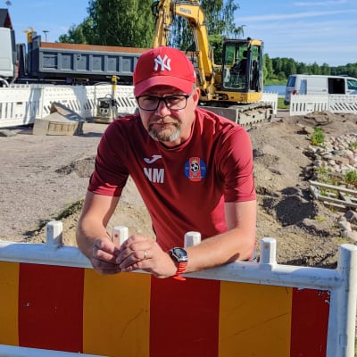 En man lutar över ett byggstaket på en arbetsplats nere vid en strand.