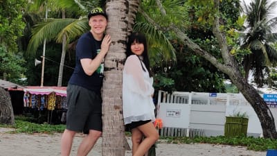 Ett par står kring en palm på en strand. 