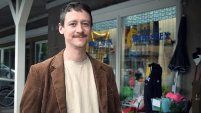 Rasmus Edlund i en brun tweedkavaj framför en prylbutik i Dalsbruk.