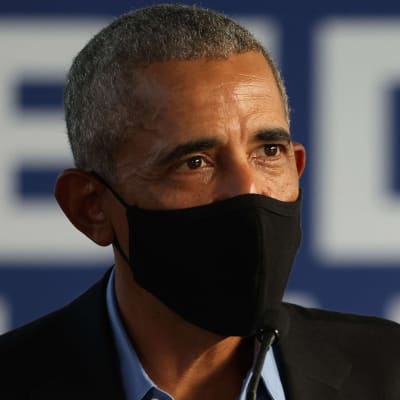 USA:s tidigare president Barack Obama talar med händerna i luften. Han har ett svart munskydd på sig.
