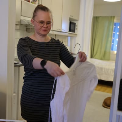 Oululainen Riitta-Liisa Kauppi laittaa vaatetta henkariin.
