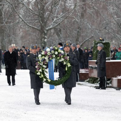 Fru jenni Haukio och president Sauli Niinistö går bakom en krans.