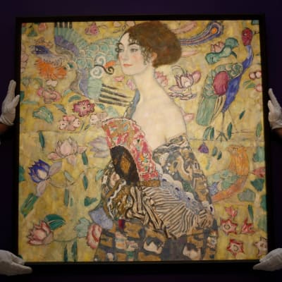 Gustav Klimts målning Dame mit Fächer. Föreställer en dam med en solfjäder. Runt henne många exotiska fåglar och blommor. Verket har mycket varma färger.