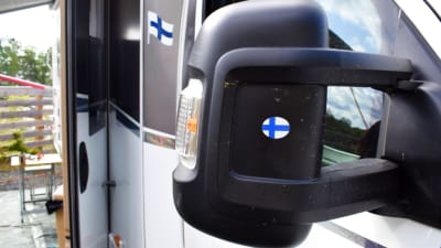 Backspegeln på en husbil med Finlands flagga påklistrad.