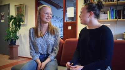 Gymnasieeleverna Hanna Gustafsson och Fanny Karell sitter i en soffa i skolkorridoren och talar med varandra.
