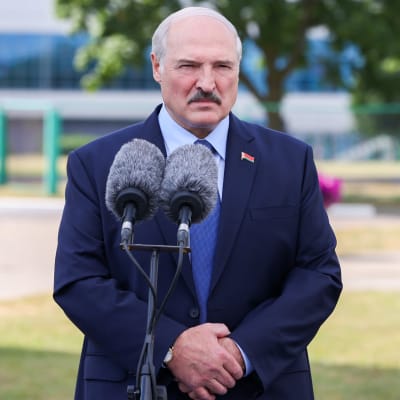 Aleksandr Lukasjenko framför mikrofoner då han talar efter röstning i val. Han har lite ljust, grått. Mörk mustasch och mörkblå kavaj. Ser sammanbiten ut.