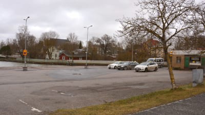 En astfaltplan med fyra bilar på, i ena hörnet ser man lilla taxihuset.
