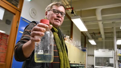 Jyri-Pekka Mikkola håller upp en flaska med det fossilfria bränslet, en klargul vätska, i ett laboratoriet.