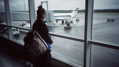 Ung kvinna tittar ut genom fönstret på flygfältets landningsbana.