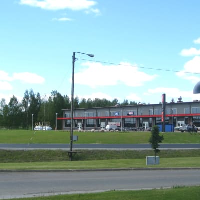 På bilden syns två vägar som har gräs på båda sidor. I bakgrunden syns en affärsfastighet.
