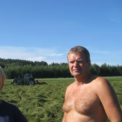 Jordbrukarna Johanna och Anders Wasström i Broby, Raseborg, I bakgrunden en traktor som fäller hö.
