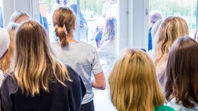 En grupp med flickor står och tittar ut genom ett fönster inne i en skola.