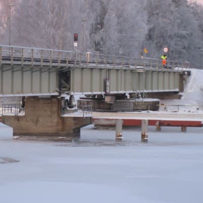 En järnvägsbro över en vik som frusit. I slutet av bron syns en man i färgglada arbetskläder.