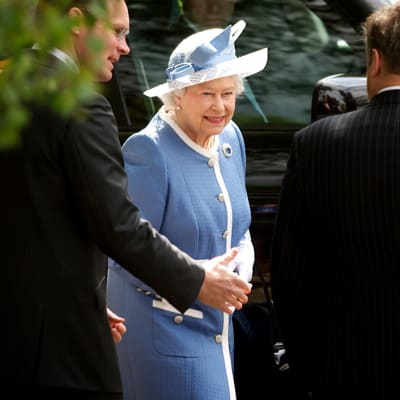 Drottning Elizabeth II ler iklädd blå klänning med kantdetaljer i vitt och matchande hatt.