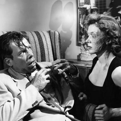 Järkyttyneen näköinen mies (Lee Marvin) katsoo naista, jonka kasvoista toinen puoli on arpeutunut (Gloria Grahame). Kuva elokuvasta Gangsterikuningas (The Big Heat, 1953).
