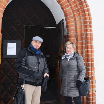 En man och en kvinna står utanför Borgå domkyrka. Kvinnan håller upp ytterdörren.