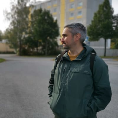 Mies seisoo kerrostalon edessä ja katsoo vasemmalle.
