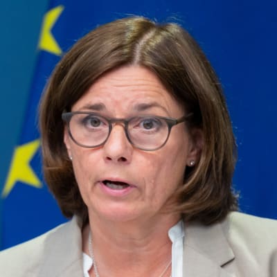 Isabella Lövin på en presskonferens med Sveriges och EU:s flaggor bakom sig.