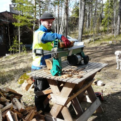 Byagårdskarlen Leif Still använder vedklyvaren i Pitkäpää medan hunden Cindy vill spela fotboll