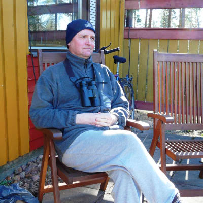 Magnus Östman, chefredaktör för Finlands natur, sitter på sin terrass och kikar på fåglar