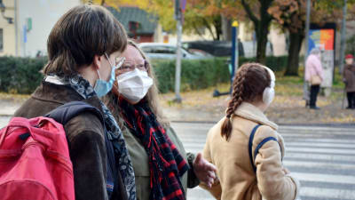 Två personer står och talar på gatan, båda har munskydd på sig.