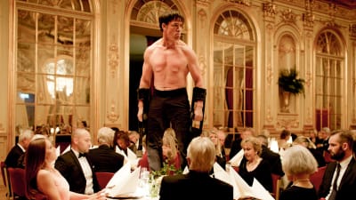 Oleg (Terry Notary) seisoo illallispöydän päällä ilman paitaa elokuvassa The Square