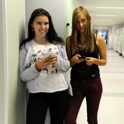 Linnéa Bäcklund och Cecilia Granlund, står med mobilerna i korridoren i högstadiet i petalax,