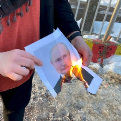 En hand som håller i en brinnade bild på Putin.